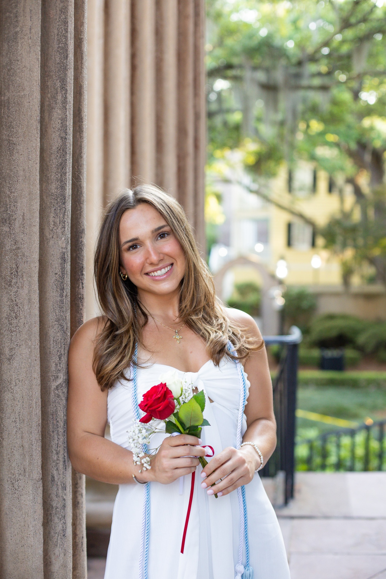 Graduate portrait with cap honor cords beside a column