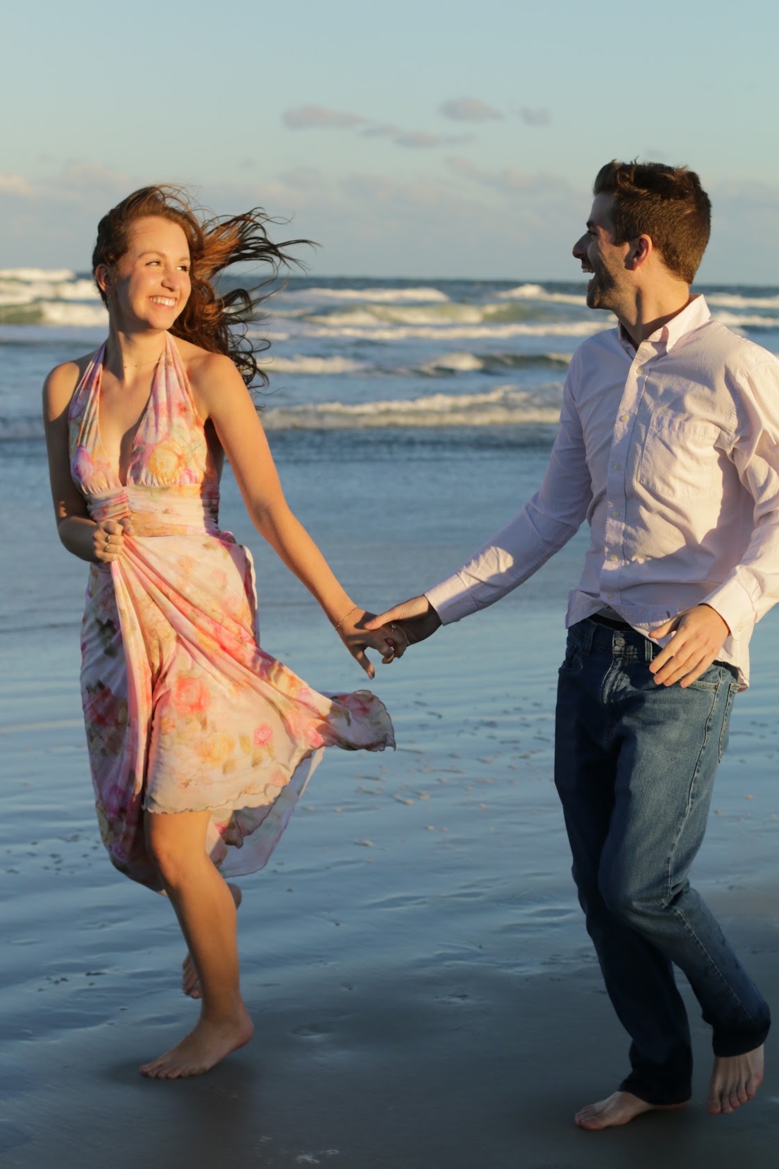 Couple holding hands and dancing barefoot on the beach at sunset