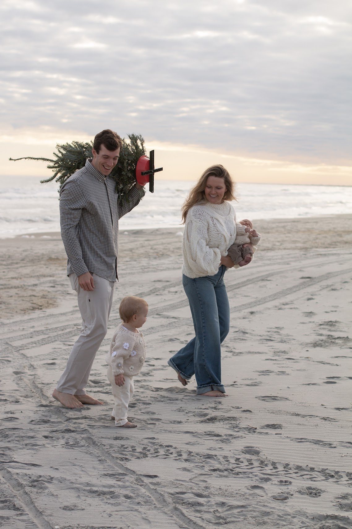 Family carrying a Christmas tree along the beach at sunset
